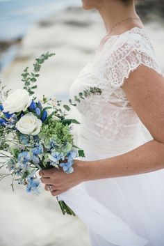 a woman holding a bouquet of white and blue flowers with greenery in her hand