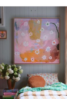 a bed sitting under a painting on the wall next to a vase filled with flowers