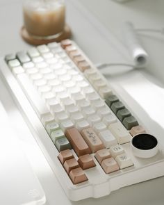 a computer keyboard sitting on top of a white desk next to a cup of coffee