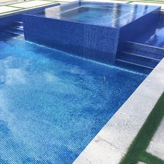 an empty swimming pool with blue tiles and green grass in the foreground, on a sunny day