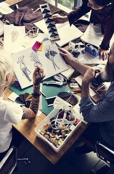 a group of people sitting around a wooden table working on drawings and paper work together