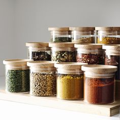 an assortment of spices and seasonings in glass jars on a shelf with wooden lids