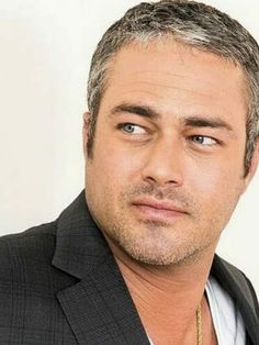 a close up of a person wearing a suit and tie with a necklace on his neck