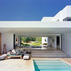 an outdoor living area with couches and tables next to a swimming pool in front of a house