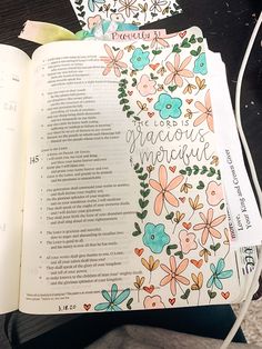 an open bible on a table with flowers and words written in the book's pages