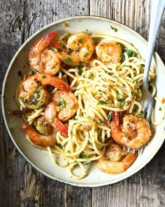 pasta with shrimp and tomato sauce in a white bowl on a wooden table next to a fork