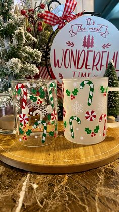 two coffee mugs with candy cane designs on them are sitting on a wooden tray