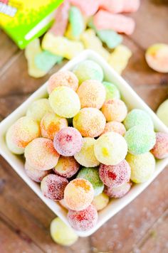 a white bowl filled with colorful candy on top of a wooden table next to a box of gummy bears