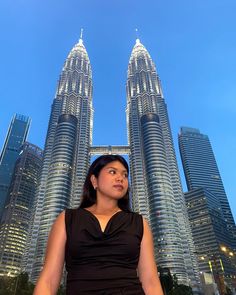 a woman is standing in front of two tall skyscrapers at night with her hands on her hips