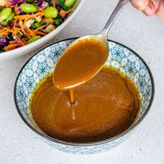 a person pouring sauce into a bowl with salad in the background