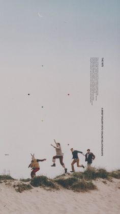 four people jumping in the air on top of a sand dune with kites flying overhead