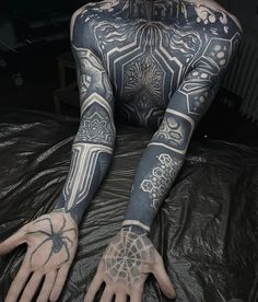 a man with tattoos on his arms and hands is laying on a black sheet in front of him