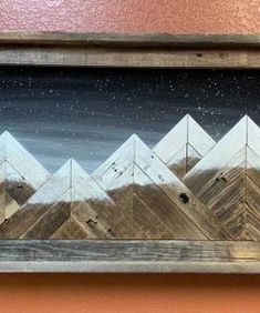 a painting with mountains and stars in the sky above it on a wooden frame hanging on a wall