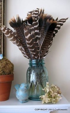 two vases filled with feathers sitting on top of a white shelf next to a potted plant