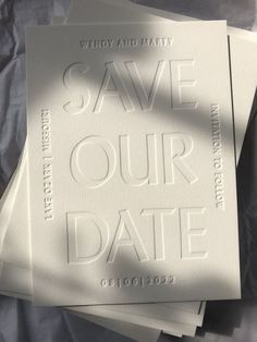 three white wedding save the dates cards on top of each other, with shadows coming from them