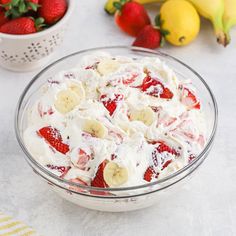 a bowl filled with strawberries and bananas on top of a table next to other fruit