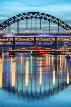 the bridge is lit up at night and reflecting in the water