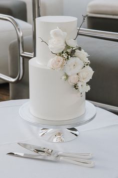 a white wedding cake with flowers and silverware on a table in front of chairs