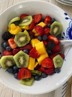 a white bowl filled with sliced fruit on top of a wooden table next to plates and utensils