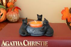 two black cats sitting on top of a book with a candle in front of it