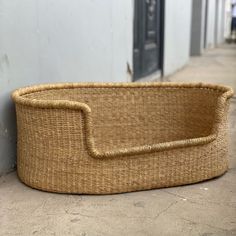 a woven basket sitting on the ground next to a wall with a door in the background