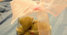 a glass jar filled with olives wrapped in a white ribbon on top of a bed