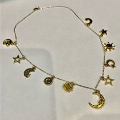 a gold necklace with various charms and stars hanging from it's sides on a white surface