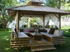 a wooden gazebo sitting in the middle of a lush green yard with lots of furniture