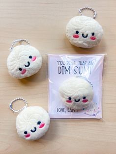 three white sheep keychains sitting on top of a wooden table next to a card