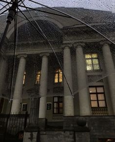 an open umbrella in front of a building with columns and windows covered by raindrops