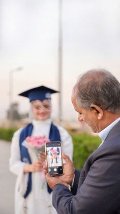 an older man holding up a cell phone to take a picture with his graduation cap and gown