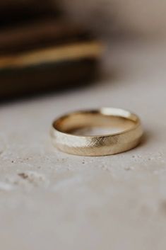 a gold wedding ring sitting on top of a white table next to a stack of books