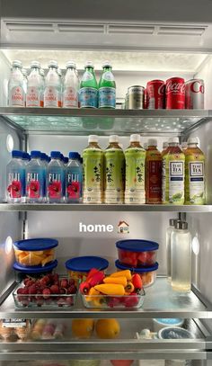 an open refrigerator filled with lots of different types of drinks and fruit in bowls on the shelves