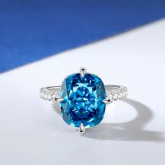 This is a stunning blue stone ring that exudes elegance and sophistication. The centre of the ring is set with a large, captivating blue stone that commands attention with its deep, enchanting hue. The sparkling centre stone is also set with a hidden halo of smaller round stones, and the glittering stone-set band adds to the brilliance of this chic ring. The smooth and delicate design ensures a comfortable fit while showcasing the beauty of the central blue stone.Carat Weight: 6.29 ctStone Size: 10*12 mmStone Type: Jeulia® StoneNumber of Stones: 1 Stone Color: Aquamarine BlueStone Shape: Fat OblongCarat Weight: 1.381 ctStone Size: 1,1.2,1.7,0.8 mmStone Type: Jeulia® StoneNumber of Stones: 68 Stone Color: Diamond WhiteStone Shape: RoundWeight: 2.9 gWidth: 1.9 mmHeight: 10 mmThickness: 1.5 m Luxury Sapphire Topaz Promise Ring, Blue Crystal Promise Ring In Fine Jewelry Style, Blue Crystal Promise Ring Fine Jewelry, Blue Open Ring Crystal Fine Jewelry, Elegant Topaz Open Crystal Ring, Blue Open Crystal Ring For Promise, Blue Crystal Open Ring For Promise, Blue Diamond Ring With Gemstone Accents, Elegant Blue Sapphire Ring, Cushion Cut