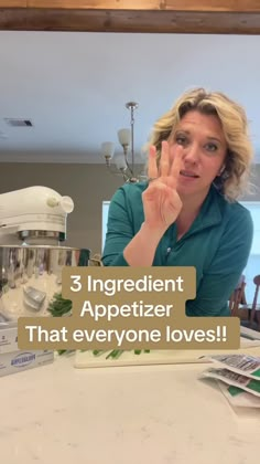 a woman sitting at a kitchen table making the peace sign with her hand and fingers