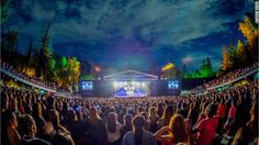 an outdoor concert is shown with the words above and above it are people standing in front of a stage