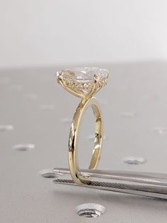 a yellow gold engagement ring with a pear shaped diamond on the side, sitting on top of a piece of metal