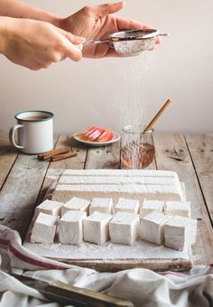 two hands sprinkling sugar onto tofu cubes on a wooden table with other ingredients