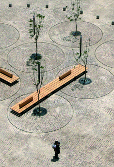 a person standing in the middle of a park with benches and trees on it's sides