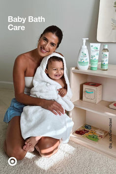 a woman holding a baby wrapped in a towel next to a shelf with personal care products