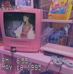 a pink tv sitting on top of a wooden table next to a cage filled with video game controllers