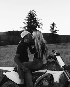 a man and woman kissing on the back of a motorbike in a field