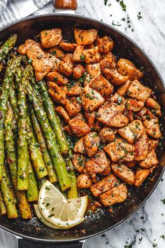 chicken and asparagus in a skillet with lemon wedges