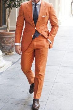 a man in an orange suit and tie walking down the street with his hands in his pockets