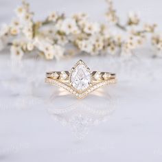 a white diamond ring sitting on top of a table next to some flowers and branches