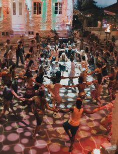 a large group of people are dancing on the floor in front of an old building