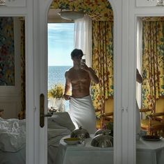 a shirtless man taking a selfie in front of a mirror next to a bed