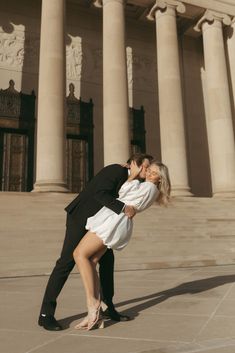 a man and woman kissing in front of an old building with columns on either side