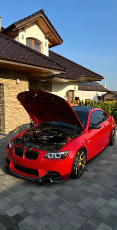 a red car is parked in front of a house with its hood open and it's engine visible