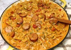 a pan filled with pasta and sausages on top of a checkered table cloth